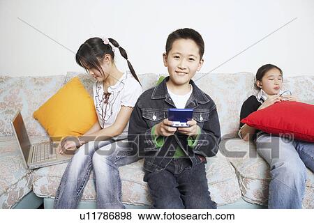 Stock Photo - Portrait of a boy playing a video game beside his two sisters. Fotosearch