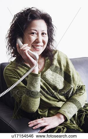 Stock Photograph - Portrait of a businesswoman sitting on a couch using a telephone. Fotosearch