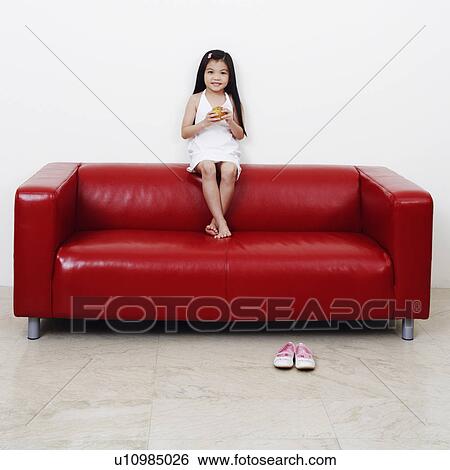 Portrait of a girl sitting on a couch and holding a burger View Large Photo Image Stock Photograph - Portrait of a girl sitting on a couch and holding a burger. Fotosearch