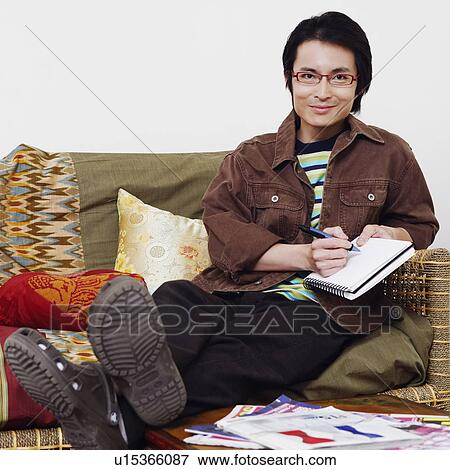 Stock Photo - Portrait of a mid adult man sitting on a couch and writing in a diary. Fotosearch