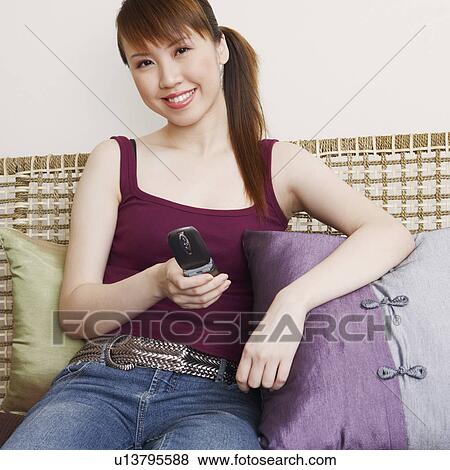 Portrait of a young woman holding a mobile phone and smiling View Large Photo Image Stock Photo - Portrait of a young woman holding a mobile phone and smiling. Fotosearch