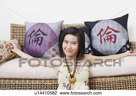 Portrait of a young woman leaning against a couch and listening to music View Large Photo Image Stock Image - Portrait of a young woman leaning against a couch and listening to music. Fotosearch