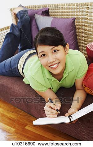 Portrait of a young woman lying on a couch and writing in a diary View Large Photo Image Stock Image - Portrait of a young woman lying on a couch and writing in a diary. Fotosearch