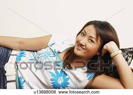Stock Photo - Portrait of a young woman lying on a couch and smiling. Fotosearch