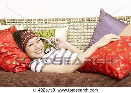 Portrait of a young woman lying on a couch and using a mobile phone View Large Photo Image Stock Photo - Portrait of a young woman lying on a couch and using a mobile phone. Fotosearch
