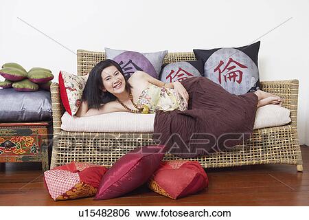 Stock Photograph - Portrait of a young woman lying on a couch and smiling. Fotosearch