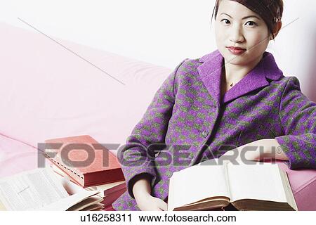 Portrait of a young woman sitting on a couch with books beside her View Large Photo Image Stock Image - Portrait of a young woman sitting on a couch with books beside her. Fotosearch