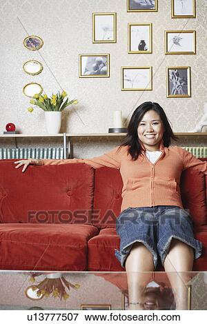 Portrait of a young woman sitting on a couch smiling View Large Photo Image Stock Photo - Portrait of a young woman sitting on a couch smiling. Fotosearch