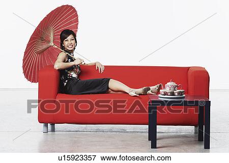 Stock Photo - Portrait of a young woman sitting on a couch holding a parasol. Fotosearch