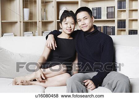Stock Photo - Portrait of a young woman sitting on a couch with a young man. Fotosearch