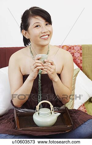Stock Image - Portrait of a young woman smiling and holding a coffee cup. Fotosearch