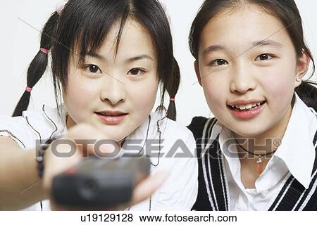 Portrait of a young woman with her sister holding a remote control View Large Photo Image Stock Photo - Portrait of a young woman with her sister holding a remote control. Fotosearch