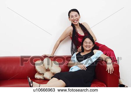 Stock Image - Portrait of two mid adult women sitting on a couch and smiling. Fotosearch