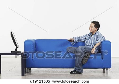 Stock Photography - Side profile of a young man holding a remote control sitting in front of a flat screen monitor. Fotosearch