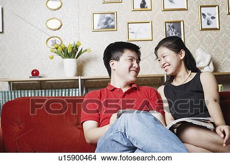 Picture - Young couple sitting on a couch looking at each other. Fotosearch