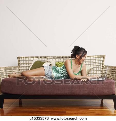 Stock Photograph - Young woman using a laptop on a couch and smiling. Fotosearch