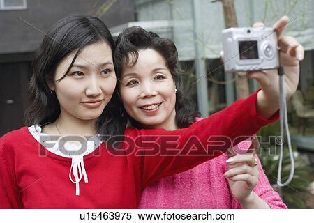 Stock Photography - Close-up of a daughter and her mother taking a photograph of themselves. Fotosearch