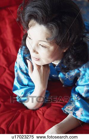Stock Photography - High angle view of a mature woman lying on the bed smiling. Fotosearch