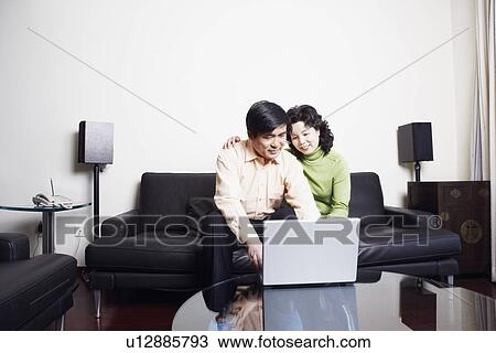 Stock Image - Mature couple sitting on a couch using a laptop. Fotosearch