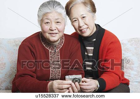Stock Photo - Portrait of a senior woman sitting on a couch with a mature woman holding a digital camera. Fotosearch