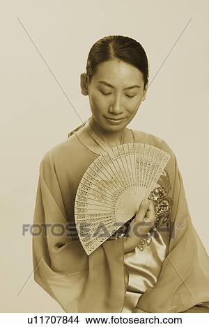 Picture - Close-up of a mid adult woman holding a folding fan with her eyes closed. Fotosearch