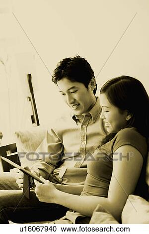 Stock Image - Close-up of a young couple looking at a picture frame and smiling on a couch. Fotosearch