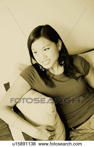 Stock Photo - High angle view of a young woman sitting on a couch and smiling. Fotosearch