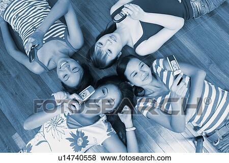 Stock Photo - High angle view of four young women lying on a hardwood floor and holding their mobile phones. Fotosearch