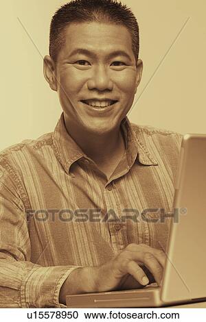 Stock Image - Portrait of a mid adult man using a laptop and smiling. Fotosearch