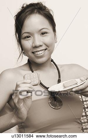 Picture - Portrait of a young woman eating biscuits. Fotosearch