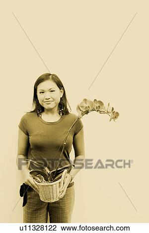 Stock Image - Portrait of a young woman holding a flower vase and smiling. Fotosearch