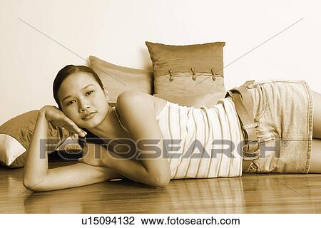Stock Image - Portrait of a young woman lying on the floor with cushions behind her. Fotosearch