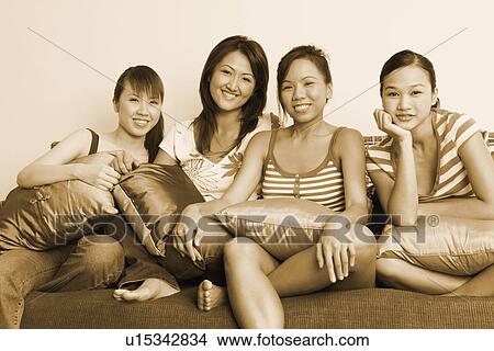 Picture - Portrait of four young women sitting on a couch and smiling. Fotosearch