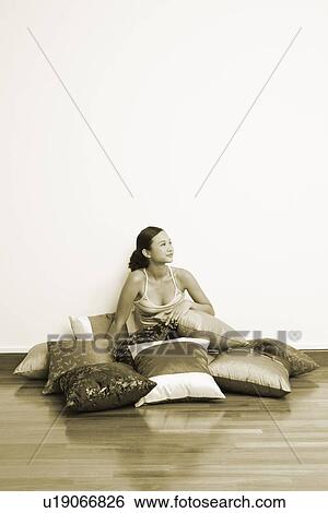 Stock Photograph - Young woman sitting on the floor with cushions. Fotosearch