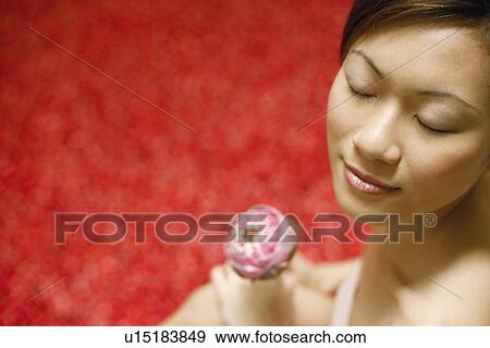 Stock Photo - Close-up of a young woman holding a flower with her eyes closed. Fotosearch