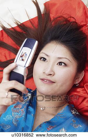 High angle view of a young woman lying on her back holding a mobile phone View Large Photo Image Stock Image - High angle view of a young woman lying on her back holding a mobile phone. Fotosearch