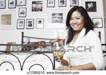 Stock Image - Portrait of a young woman holding a glass of wine smiling. Fotosearch