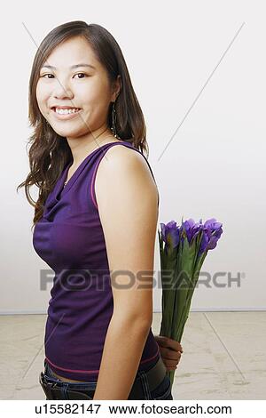 Portrait of a young woman holding a bouquet of flowers behind her back View Large Photo Image Stock Photo - Portrait of a young woman holding a bouquet of flowers behind her back. Fotosearch