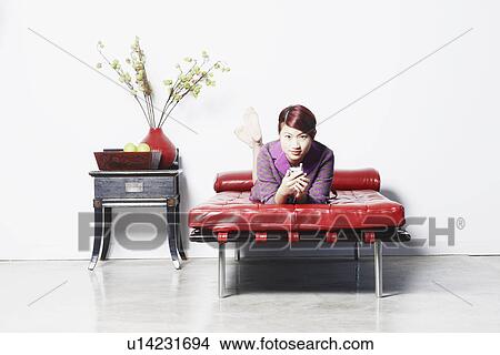 Portrait of a young woman lying on the bed holding a mobile phone View Large Photo Image Picture - Portrait of a young woman lying on the bed holding a mobile phone. Fotosearch