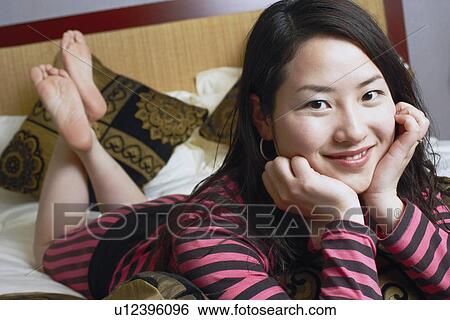 Stock Photograph - Portrait of a young woman lying on the bed smiling. Fotosearch
