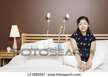 Stock Photo - Portrait of a young woman sitting on the bed smiling. Fotosearch