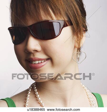 Stock Photography - Close-up of a young woman wearing sunglasses and smiling. Fotosearch