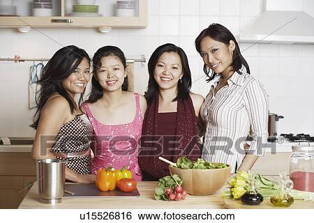 Stock Photograph - Portrait of a mid adult woman standing with three young women in the kitchen. Fotosearch