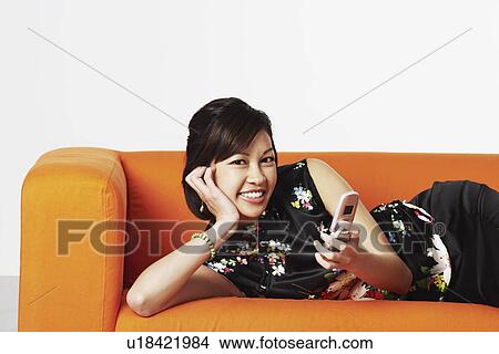 Picture - Portrait of a young woman lying on a couch smiling. Fotosearch