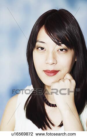 Stock Image - Portrait of a young woman smiling with her hand under her chin. Fotosearch