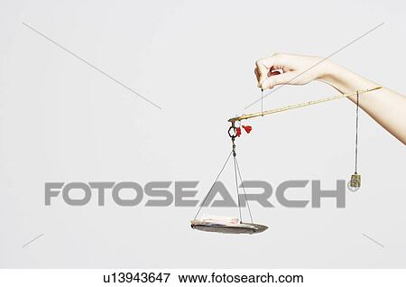 Stock Photo - Close-up of a person's hand holding a weighing scale with paper currency. Fotosearch