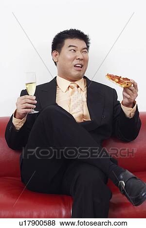 Close-up of a businessman sitting on a couch holding a slice of pizza with a champagne flute View Large Photo Image Stock Photo - Close-up of a businessman sitting on a couch holding a slice of pizza with a champagne flute. Fotosearch