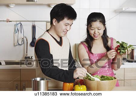 Stock Image - Close-up of a young man and a mid adult woman preparing food. Fotosearch