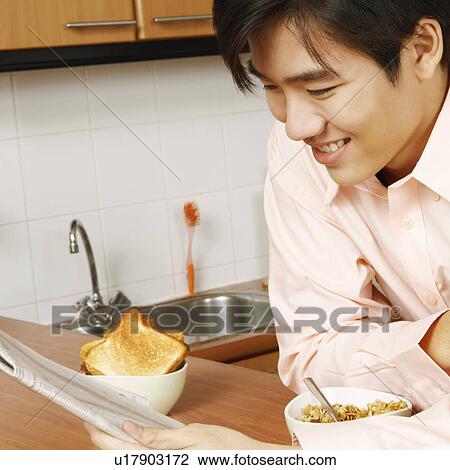 Stock Image - Close-up of a young man reading a newspaper at a kitchen counter. Fotosearch