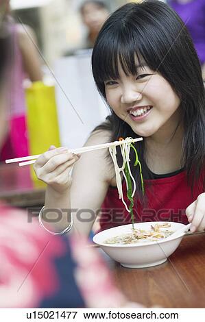 Stock Photo - Close-up of a young woman eating noodles with chopsticks. Fotosearch